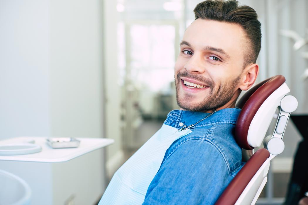 Happy man with hazel eyes and dark brown hair is sitting in dental chair and smiling