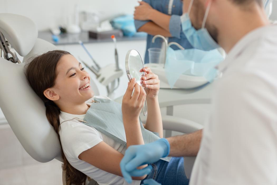 girl looking in the mirror after a sealant treatment at the dentist's office