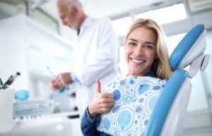 Happy young woman with perfect smile after dental exam showing a thumb up.