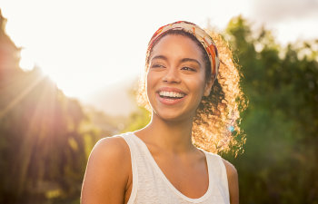 joyful girl with headband in hair laughing against the trees and sunset