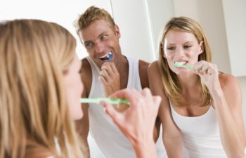 Woman brushing her teeth while man is applying deodrant